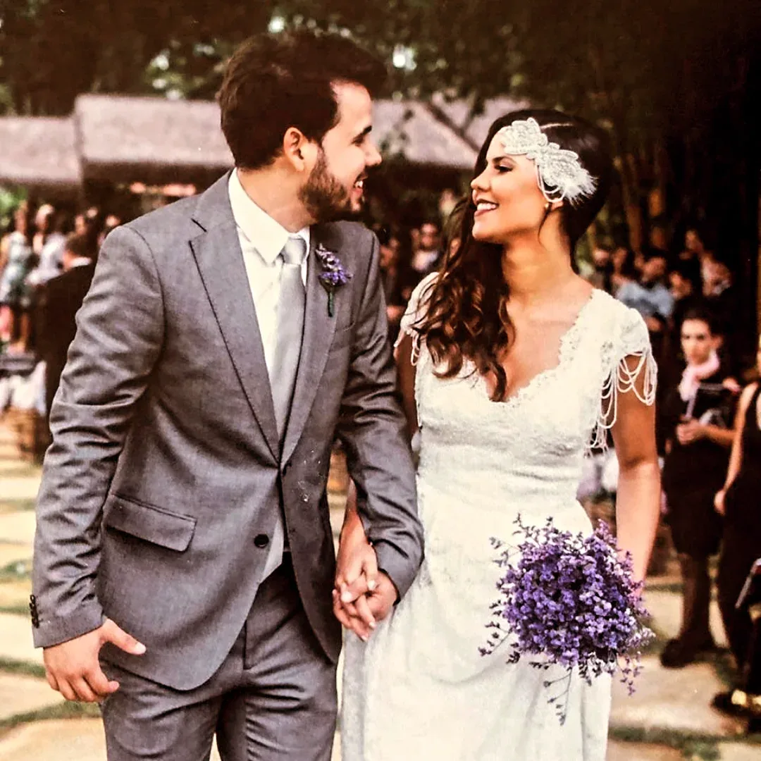Casal de noivos caminha de braços dados e troca sorrisos durante uma cerimônia.