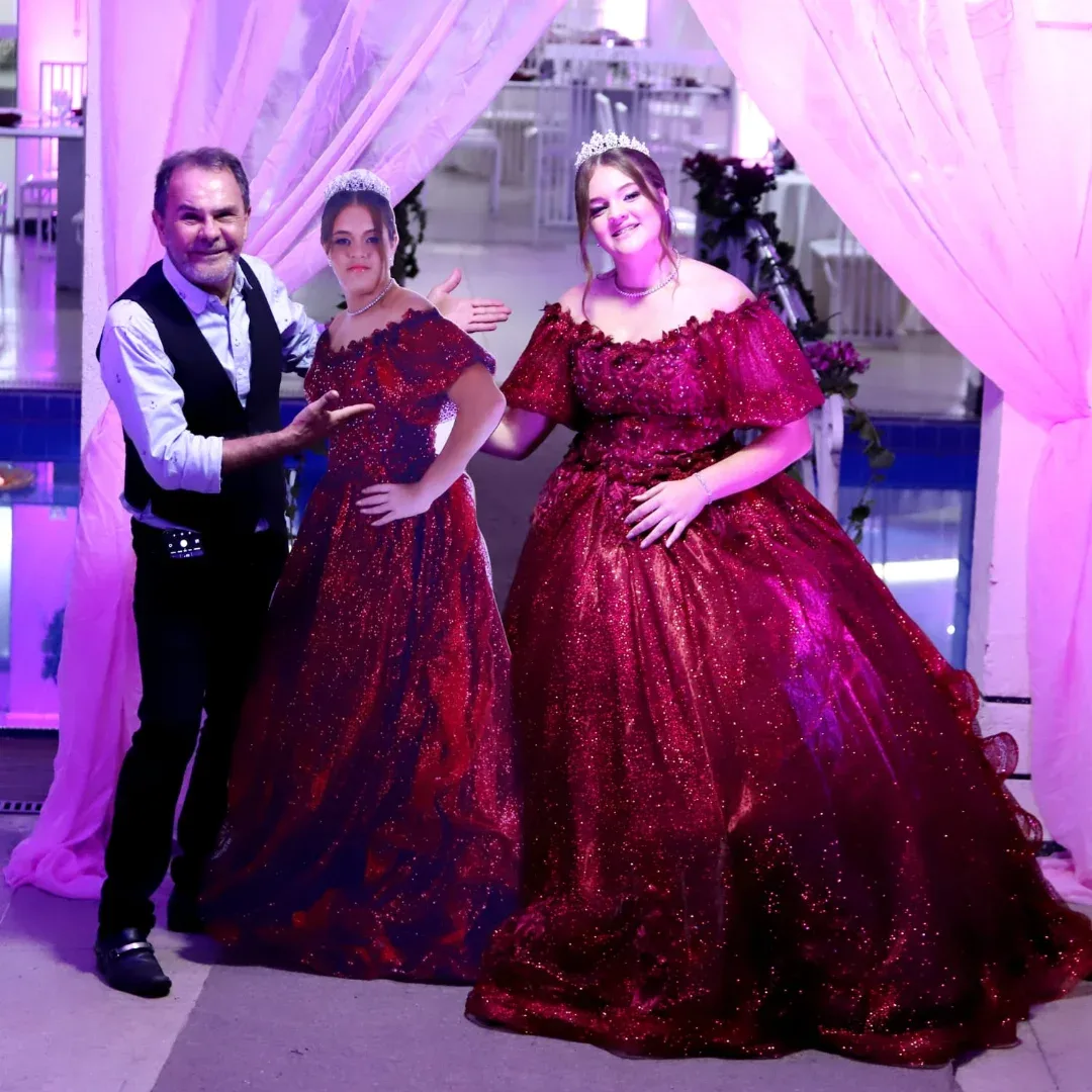 Homem e duas mulheres posam juntos diante de uma decoração de festa iluminada em lilás.