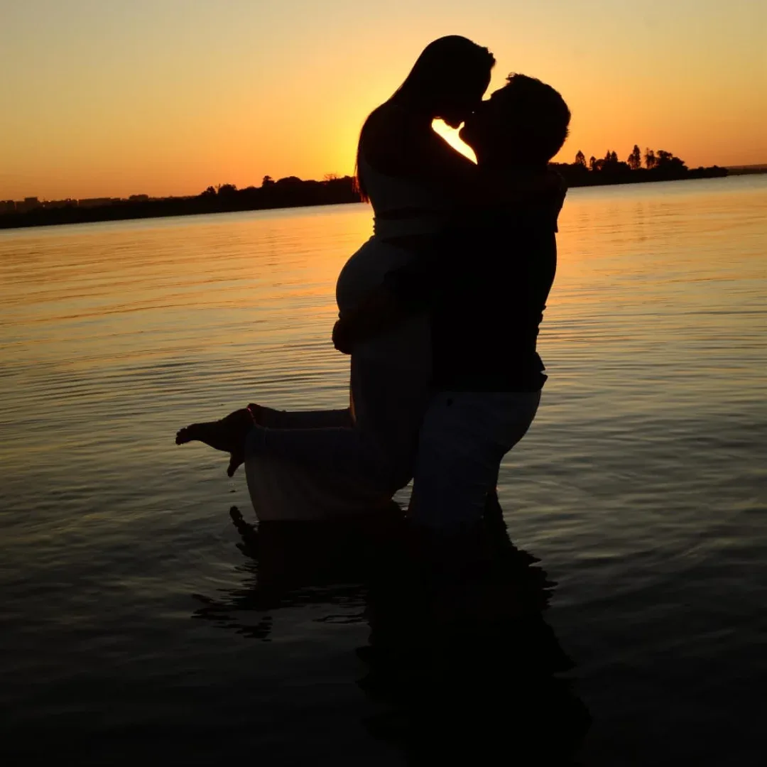Silhueta de um casal abraçado dentro da água ao pôr do sol.