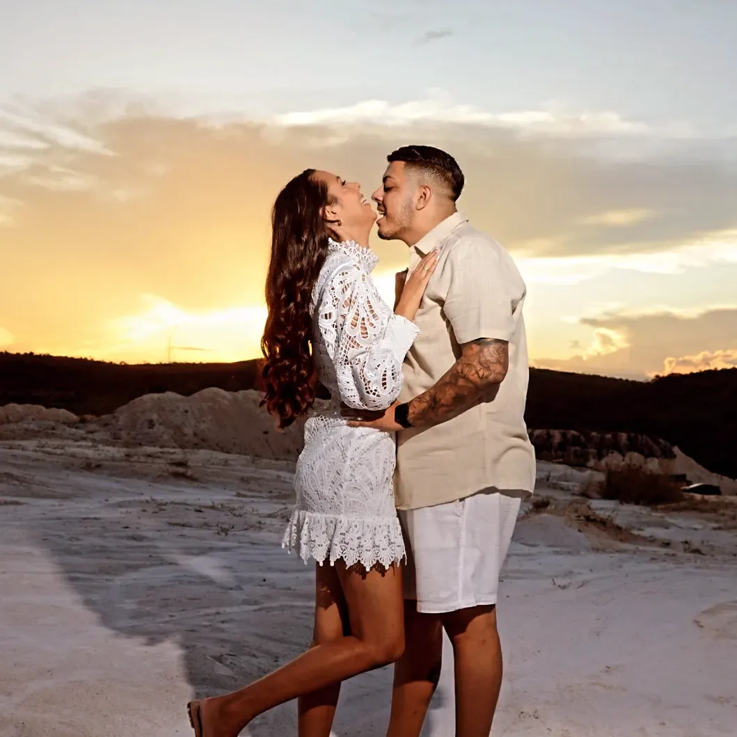 Casal se abraça diante de uma paisagem ao pôr do sol.
