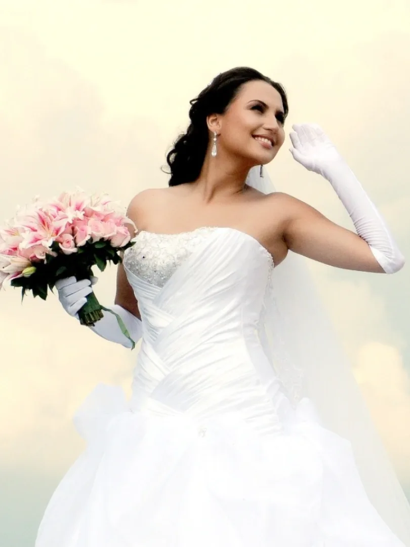 Noiva de vestido branco segura um buquê rosa em um jardim.