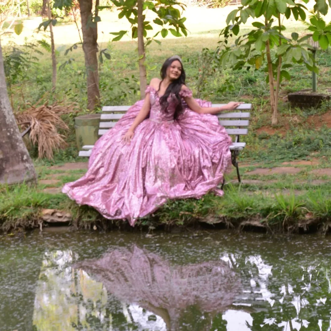 Mulher de vestido rosa sentada à beira de um lago, com reflexo na água.