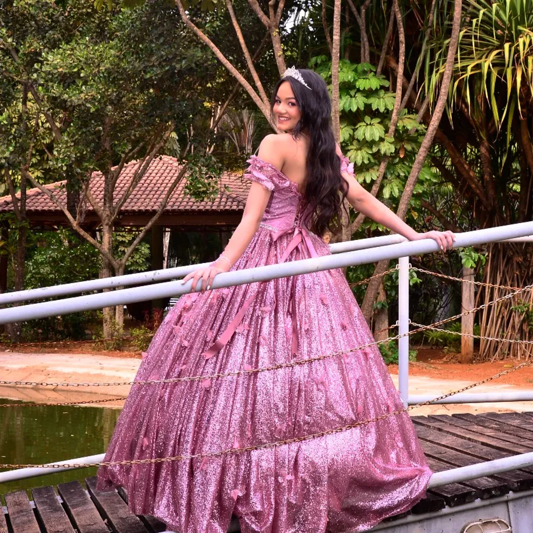 Mulher de vestido rosa sobre uma ponte de madeira cercada por vegetação.